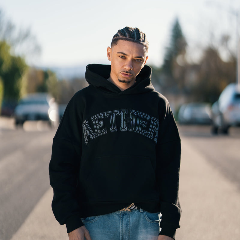 Person wearing a black hoodie with 'Aether' branding on a road.